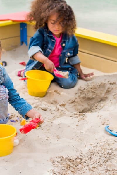 three multiethnic little children playing with plastic scoops and buckets in sandbox at playground