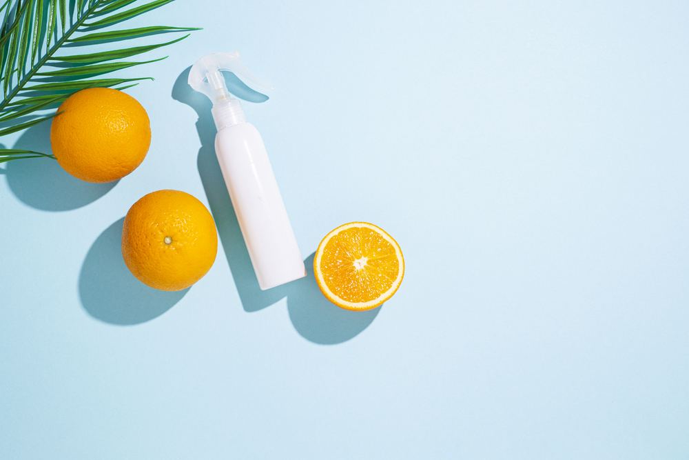 spray bottle, oranges and a leaf of a palm tree on a blue background. Top view, flat lay.