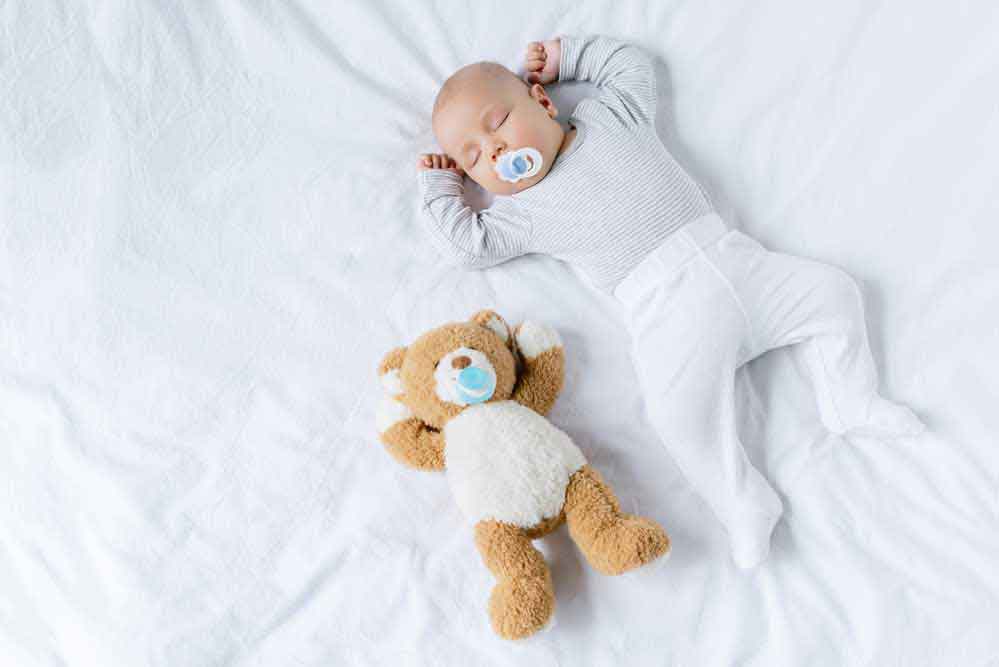 Newborn sleeping on a bed with teddy bear