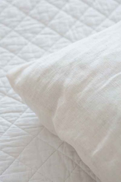 A white pillow on a white quilted sheet