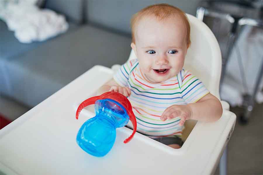 Baby smiling in white high chair with blue and red sippy cup