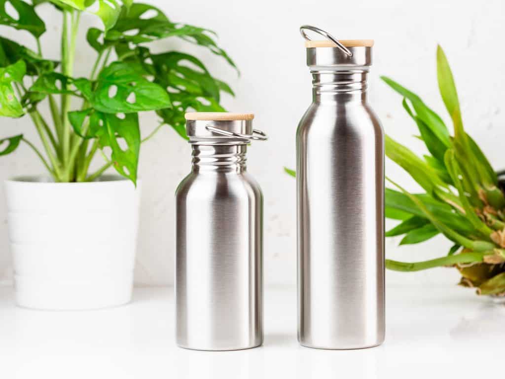 Two stainless steel eco-friendly water bottles of different sizes on the table with houseplants on the background